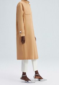 Beżowy płaszcz sięgający do kolan z wysokim kołnierzem i bocznymi kieszeniami. Srebrne guziki na mankietach. Nosi się go na białych, krótkich spodniach i srebrnych szpilkach.