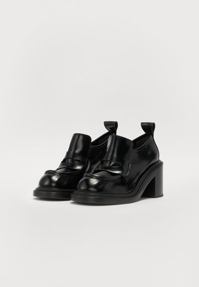Scarpe nere in pelle con tacco, dalla punta arrotondata, dotate di un dettaglio con cinturino frontale e linguette sul retro. Texture liscia e tacco robusto.