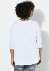 Tunique blanche à manches longues, coupe ample, encolure ronde et ourlet légèrement incurvé, réalisée en tissu léger et texturé.