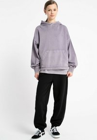 Przesadzony fioletowy hoodie z przednią kieszenią, żebrowanymi mankietami i dołem, w połączeniu z luźnymi czarnymi spodniami i czarnymi trampkami.