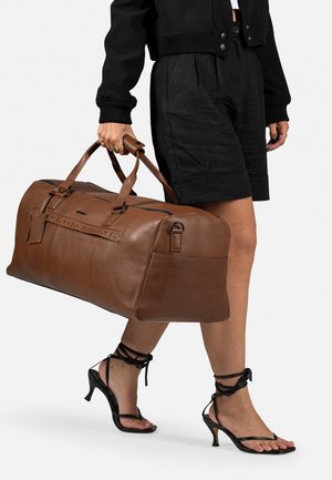 Bruine leren reistassen met stevige handvatten, rechthoekige vorm, gegraveerde tekst aan de zijkant en een ritssluiting.