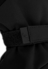 Schwarzer Stoff mit einer strukturierten Oberfläche, ausgestattet mit einem Klettverschluss und einem rechteckigen Plastikelement. Das Design ist einfach und funktional.
