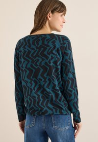 Top met lange mouwen in teal en zwart, met een abstract zigzagpatroon. Gemaakt van zachte stof met een ontspannen pasvorm en een ronde halslijn.