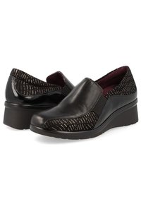 Zapatos negros tipo slip-on con un patrón texturizado, confeccionados con materiales de cuero y sintético, y un tacón bajo en cuña. El interior cuenta con un forro burdeos.