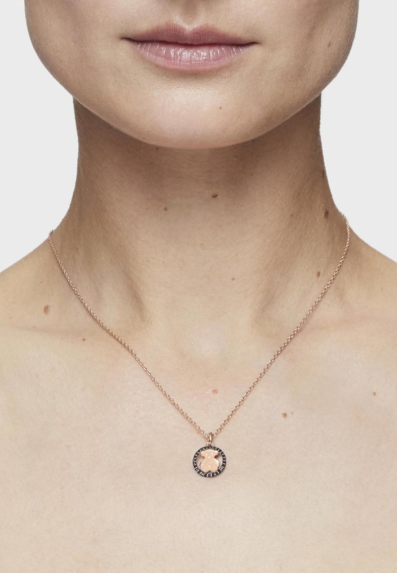 Collar de oro rosado con un colgante redondo que presenta un diseño texturizado y un borde de piedra negra, suspendido de una cadena fina.