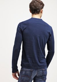 Námořnické triko s dlouhým rukávem z hladkého, lehkého materiálu. Vybaveno kulatým výstřihem a přiléhavými rukávy. Nosí se s modrými džíny.