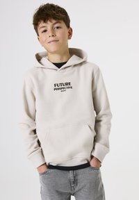 Sudadera con capucha color beige claro, con bolsillo frontal, texto negro "PERSPECTIVA DEL FUTURO" centrado en el pecho, combinada con jeans grises.