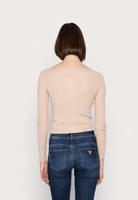 beige gerippter Langarmtop mit weit ausgeschnittenem Hals, kombiniert mit dunkelblauen engen Jeans mit Gesäßtaschen und einem Dreiecksakzent.