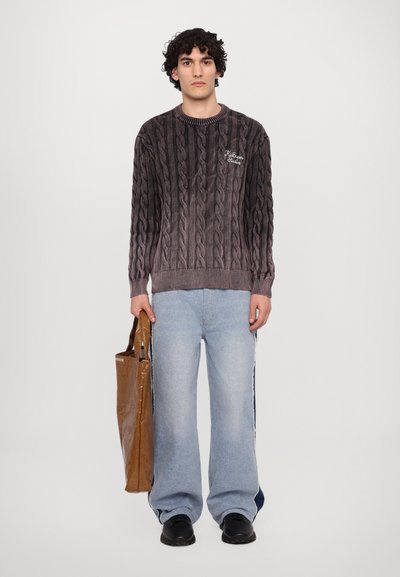Pull en tricot à mailles torsadées dégradé de gris, avec un col rond et des détails brodés. Accompagné d'un jean bleu clair large et d'un sac tote marron.