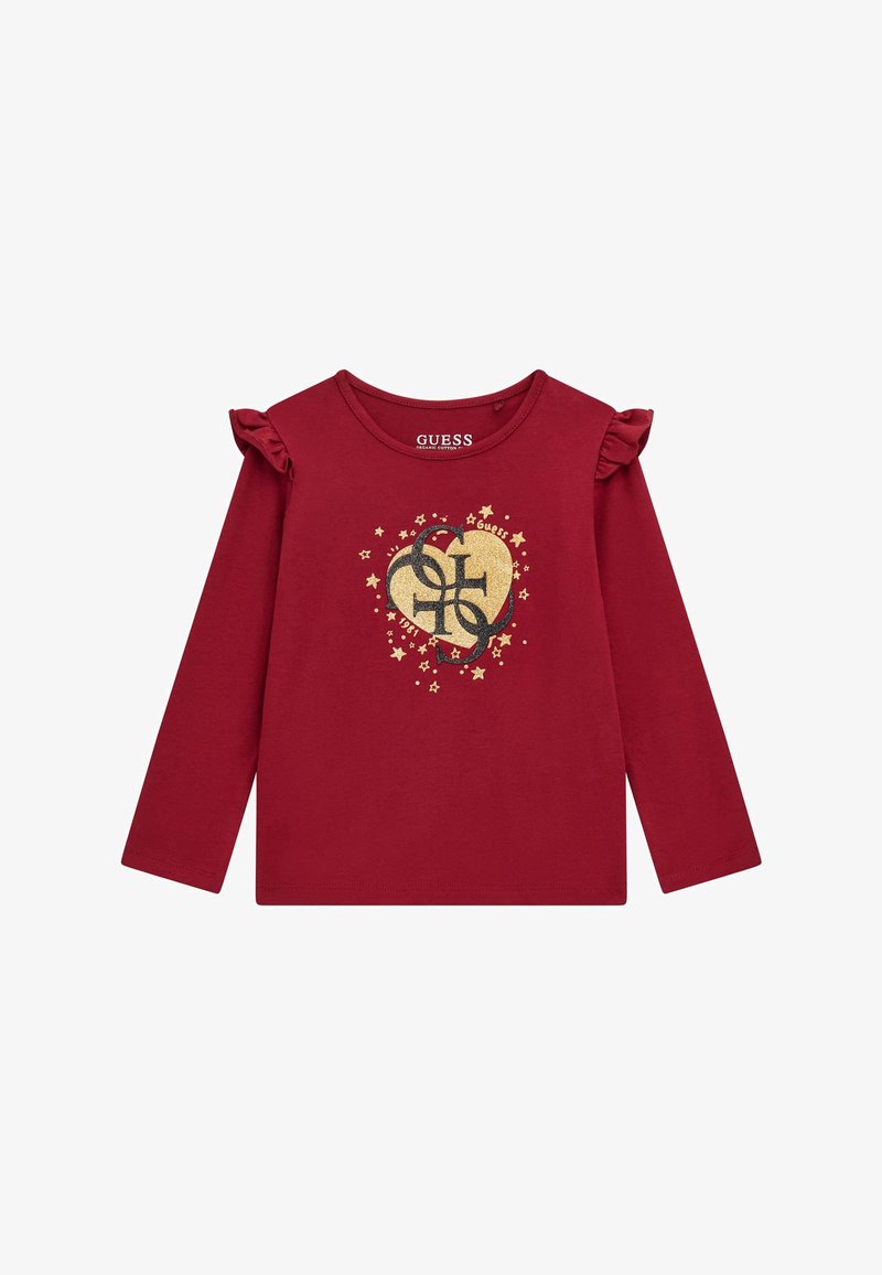 Camiseta de algodón roja de manga larga que presenta acentos de volantes en las mangas, un logo de corazón dorado con estrellas y el nombre de la marca "GUESS" impreso en el interior.