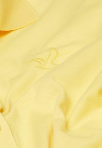 Gelbes Gewebe mit einer strukturierten Oberfläche, das ein dezentes gesticktes Logo-Detail aufweist.