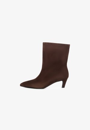 Bottine en daim marron avec un bout pointu et un petit talon fin. Présente une texture lisse et une silhouette ajustée pour un look épuré.