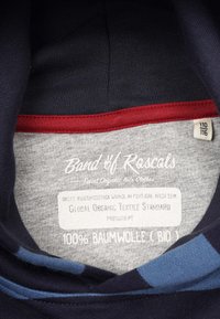 Mörkblå bomullsskjorta med en grå innervarv, som har en röd accent och etikett som indikerar ekologisk bomull och produktionsstandarder.