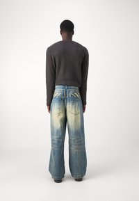 Oversized light blue denim jeans with a faded effect and unique stitching details at the back, paired with a dark knitted sweater.