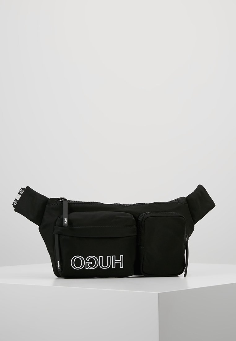 Banane en tissu noir avec deux compartiments zippés, logo blanc « HUGO » sur la poche avant et sangle réglable avec étiquettes logo.