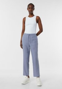 Hellblaues geripptes Tanktop kombiniert mit hellgrauen Jogginghosen mit Kordelzug und zwei Fronttaschen. Die Sneakers sind weiß mit einer strukturierten Oberfläche.