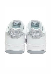 Pāra baltu sporta apavu ar pelēku rakstainu papēžu cilpām, baltu izšūtu logotipu un mīkstinātām potītes apkaklēm, attēlotas no aizmugures.