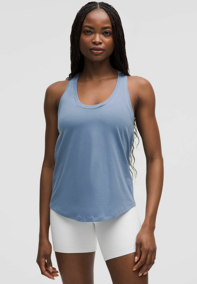 Jasnoniebieski bezrękawnik z dekoltem w serek; miękki materiał, luźny krój i zaokrąglony dół, zestawiony z białymi dopasowanymi szortami.