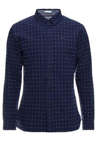 Tmavě modrá košile s dlouhým rukávem, bílým vzorem diamantů, límcem na knoflíky, knoflíky vpředu a malým logem na hrudi.
