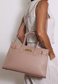 Borsa in pelle rosa con due manici superiori e una tracolla staccabile. Presenta hardware dorato e una finitura testurizzata.