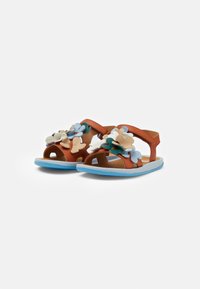Sandalias de cuero marrón con apliques florales en azul, crema y verde. Tienen la punta abierta, correas ajustables y una suela de color azul claro.