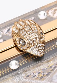 Clutch in acrilico trasparente con una chiusura dorata a forma di rana, abbellita da strass e un motivo geometrico sottostante.