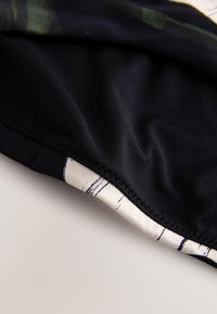 Gros plan d'un tissu noir avec un ourlet cousu et une petite section de matériau blanc à motifs en dessous.
