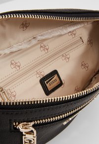 Indvendig i en sort læder håndtaske med beige foring, der har en lynlåslomme, gyldent hardware og et brandet mærke. Diskret logomønster til stede.