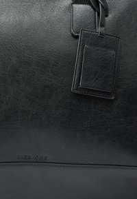 Sac en cuir noir avec une texture lisse, de forme rectangulaire, et une étiquette bagage attachée. Nom de la marque "PIER ONE" embossé en bas.