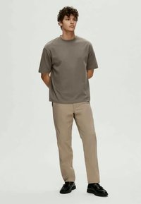 T-shirt cinza de manga curta combinado com calças bege e sapatos pretos. O t-shirt tem um corte solto e um decote redondo, com uma textura suave.