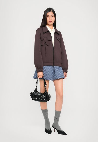 Σκοτεινά μωβ ζακέτα με φλοράλ λεπτομέρεια, ανοιχτόχρωμο πουκάμισο, μπλε καρό φούστα, γκρι κάλτσες και μαύρη τσάντα με καρφιά και αγκράφες.