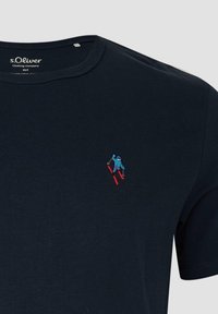 T-shirt bleu marine avec un skieur brodé portant une veste bleue et des skis rouges sur le côté gauche de la poitrine, étiquette de la marque s.Oliver à l'intérieur du col.