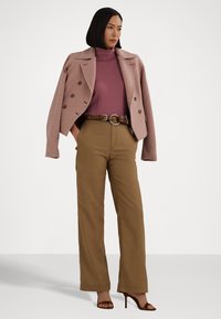 Divreiz valkāts rozā vilnas bleizeris virs pieguļošas purpursarkanās turtleneckas, apvienots ar augstā vidukļa brūnajām biksēm un brūnām papēžu sandālēm.