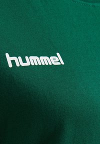 Zielona bawełniana koszulka z teksturowanym wykończeniem, okrągłym dekoltem i białym nadrukiem logo "hummel" na przodzie.
