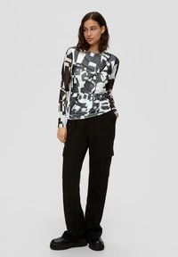 Langarmtop met een zwart-wit geometrisch patroon, met een aansluitend ontwerp en doorschijnende mouwen, gecombineerd met high-waisted cargo broeken.