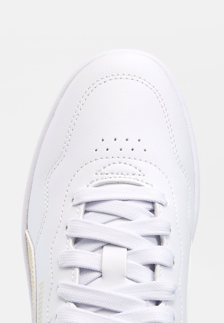 Gros plan de la partie avant supérieure d'une basket blanche avec des lacets blancs croisés et de petits détails de perforation sur la zone des orteils.