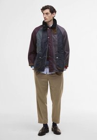 Vízálló dzseki sötét színek keverékével, többek között bordóval és zölddel. Gombos lezárása van, két elülső zsebe és szőrmebéléses gallérja.