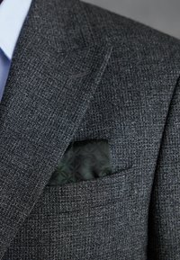 Sacou texturat de culoare gri închis cu un model subtil; are un batic negru cu un model, vizibil în buzunarul de la piept.