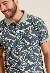 Korte mouwen polo shirt in een katoenmix met een groen loofpatroon op een crèmekleurige achtergrond. Voorzien van een gestreepte kraag en een twee-knoopsluiting.