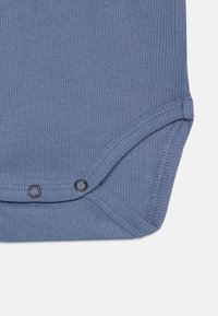 Blå ribbad bodysuit med tryckknappar längst ner, med en slät textur och rundade kanter, designad för komfort och enkelhet.