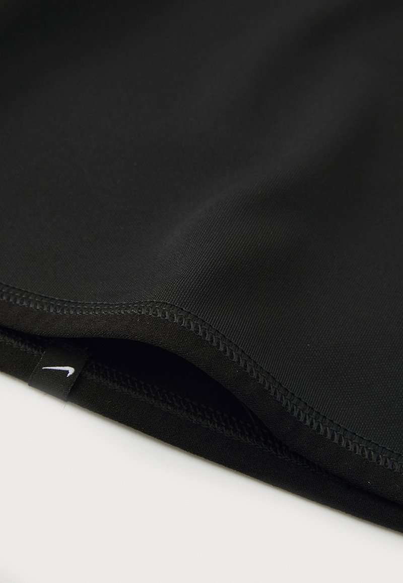Tissu de sport noir avec une texture lisse, présentant des bords cousus. Une petite étiquette blanche avec le logo Nike est visible près de l'ourlet.