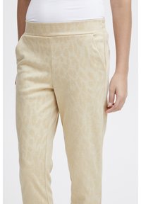 Beżowe spodnie dresowe wykonane z miękkiego materiału, z delikatnym wzorem w panterkę, bocznymi kieszeniami oraz elastycznym paskiem w talii.