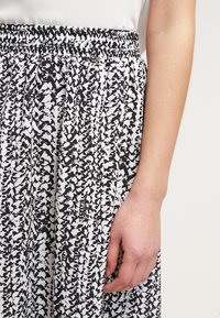Svart och vit mönstrad kjol med elastisk midja, med en texturerad yta och ett flödande mönster, delvis visad med en hand.