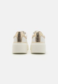 Baskets plateformes blanches avec une texture reptile dorée brillante au talon et un design lisse et épuré. Semelle en caoutchouc blanche épaisse.