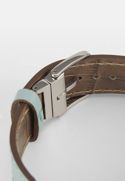 Braunes Lederarmband mit silberner Metall-Dornschließe und hellblauer Lederlasche, teilweise geöffnet auf weißem Hintergrund gezeigt.