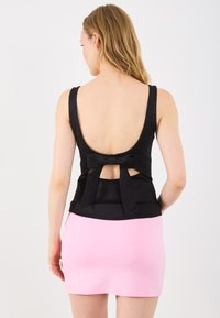 Top nero senza schienale con spalline larghe e dettaglio a fiocco sul retro, abbinato a una mini gonna rosa aderente.