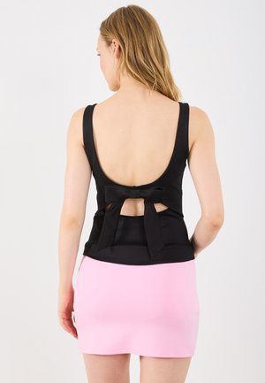 Black backless top with wide straps and a bow detail at the back, paired with a fitted pink mini skirt.