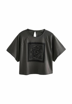 Dark gray short-sleeved top with a wide neckline, featuring a textured black square patch at the front and scalloped trim along the hem.