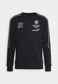 Sudadera negra con cuello redondo, mangas largas, ribetes blancos y parches bordados coloridos con logotipos y diseños en la parte frontal.