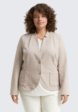 Blazer beige chiaro con una texture liscia, colletto a scollo a V, due tasche frontali e due bottoni sul davanti, indossato sopra una maglietta bianca.